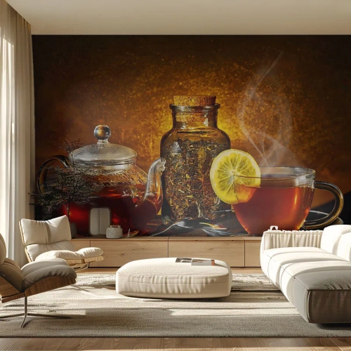 Fototapete Premium Sand - Eine Glaskanne und eine Tasse Tee mit Zitrone auf goldenem Hintergrund. - 100x70cm - Im Stil der niederländischen Meister - Moderne Wanddekoration für Wohnzimmer und Schlafzimmer ARTTOR