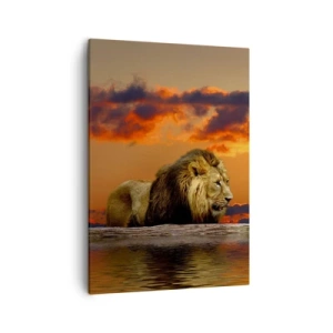 Bild auf Leinwand - Leinwandbild - Ein Löwe ruht bei Sonnenuntergang vor einem dramatischen Himmel am Wasser. - 50x70cm - König der Natur - Moderne Wanddekoration für Wohnzimmer und Schlafzimmer ARTTOR