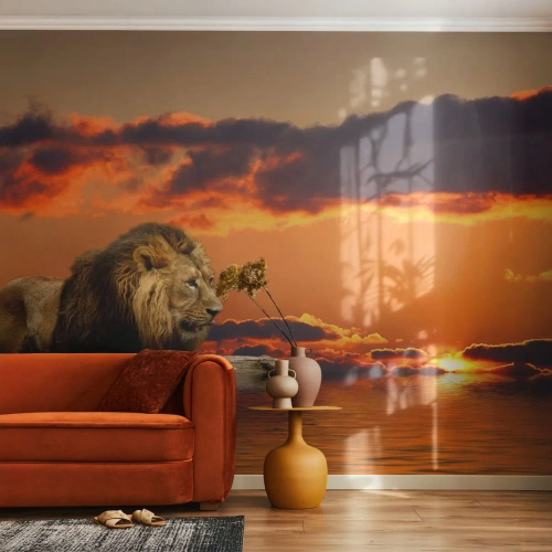 Fototapete Standard Eco - Ein Löwe ruht auf einem Felsen, während die Sonne über dem Wasser untergeht. - 100x70cm - König der Natur - Moderne Wanddekoration für Wohnzimmer und Schlafzimmer ARTTOR