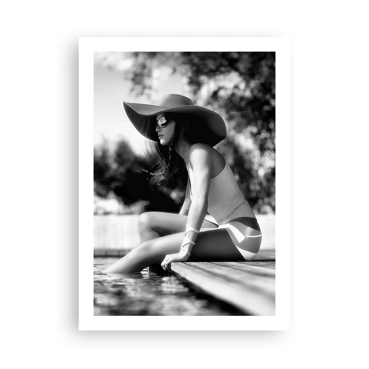 Poster - Ein Schwarzweißfoto einer Frau mit Hut, die am Wasser sitzt. - 50x70cm - Sommertraum - Moderne Wanddekoration für Wohnzimmer und Schlafzimmer ARTTOR