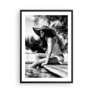 Poster in einem schwarzem Rahmen - Ein Schwarzweißfoto einer Frau mit Hut, die am Wasser sitzt. - 50x70cm - Sommertraum - Moderne Wanddekoration für Wohnzimmer und Schlafzimmer ARTTOR